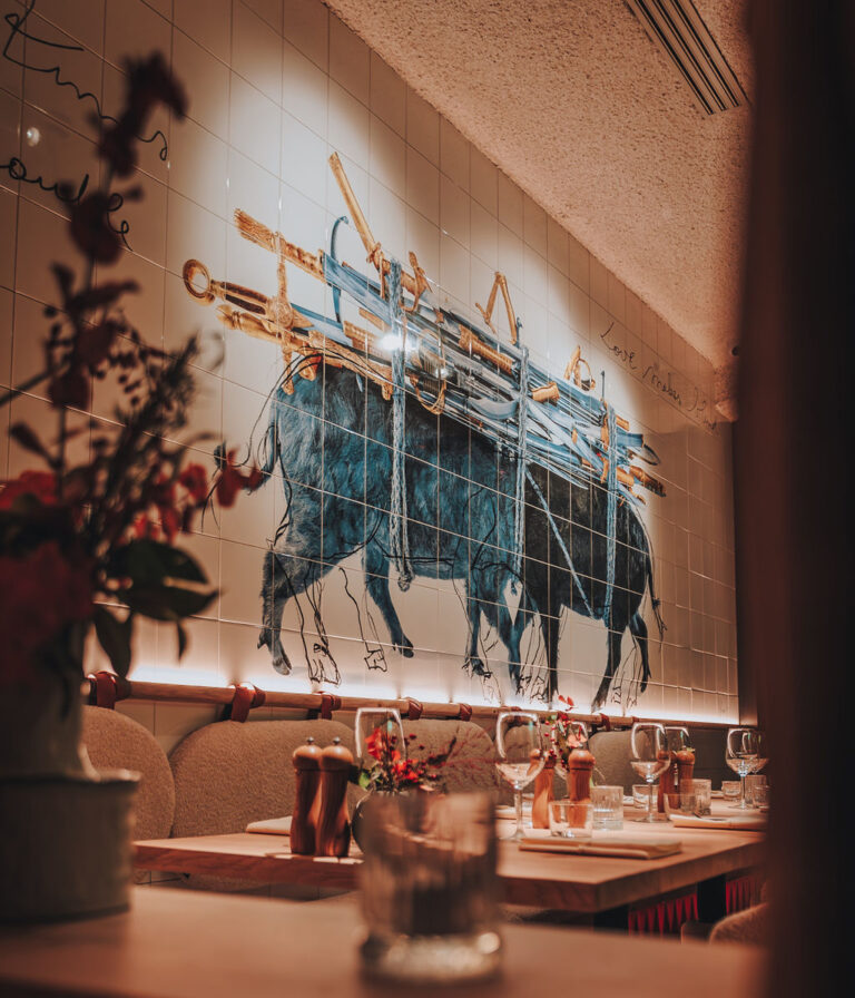 Interieur van Lucy’s Table met kunstwerk van ossen boven sfeervol gedekte tafels