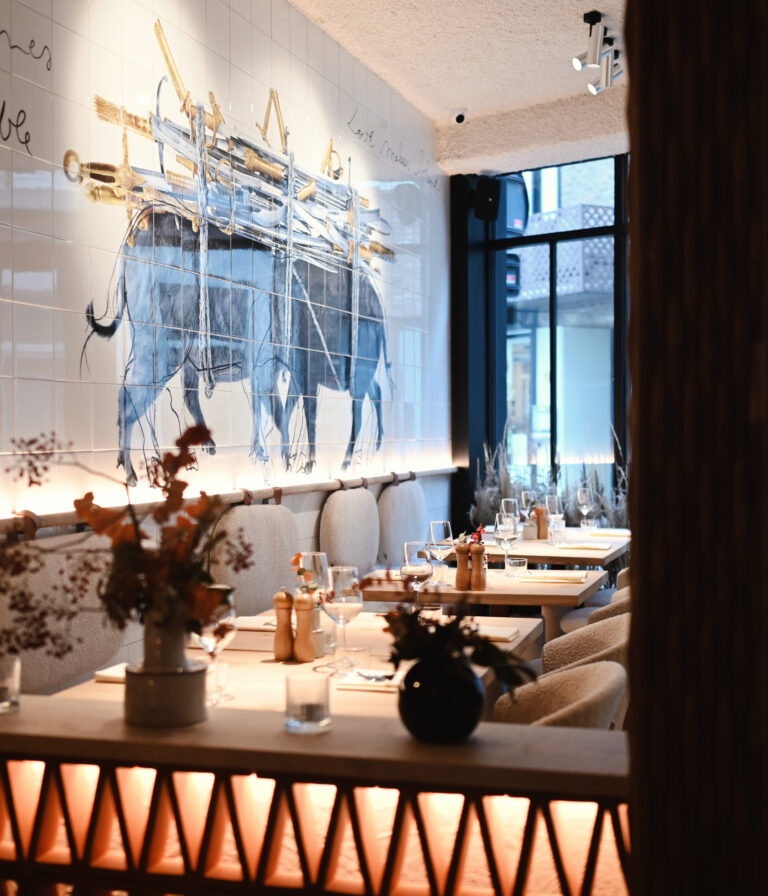 estauranttafels bij raam in Lucy’s Table met kunstwerk en warme verlichting